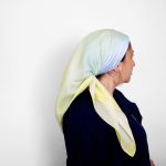 Hand-painted silk scarf in soft sky-inspired gradients of blue, green, and yellow, shown floating in the air and worn as a Jewish head covering (tichel)