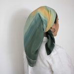 Hand-painted green silk headscarf with abstract yellow and blue patterns, displayed flat and worn as a Jewish hair covering.