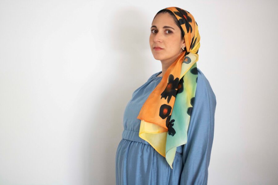 Hand-painted silk headscarf with large black flowers over a gradient orange-yellow-aqua background, ideal for modest Jewish hair covering.
